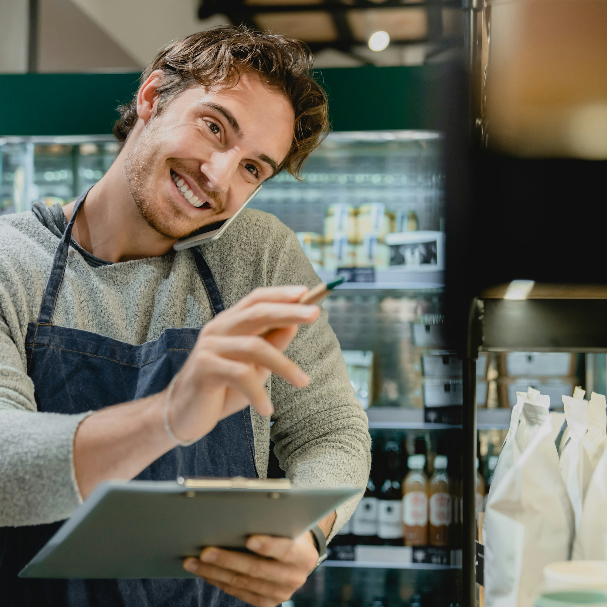 Cropped portrait of young handsome barista talking on the phone with notepad in his hands